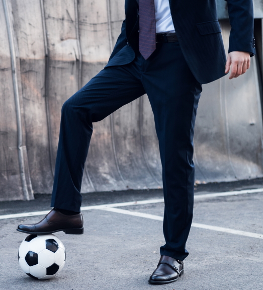 partial view of businessman in suit playing soccer on street