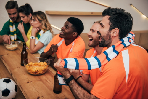 side view of happy young multicultural friends in orange fan t-shirts celebrating goal in soccer